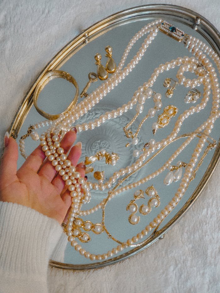 about-04 A collection of vintage pearls and gold jewelry elegantly displayed on a silver tray for a luxurious look.
