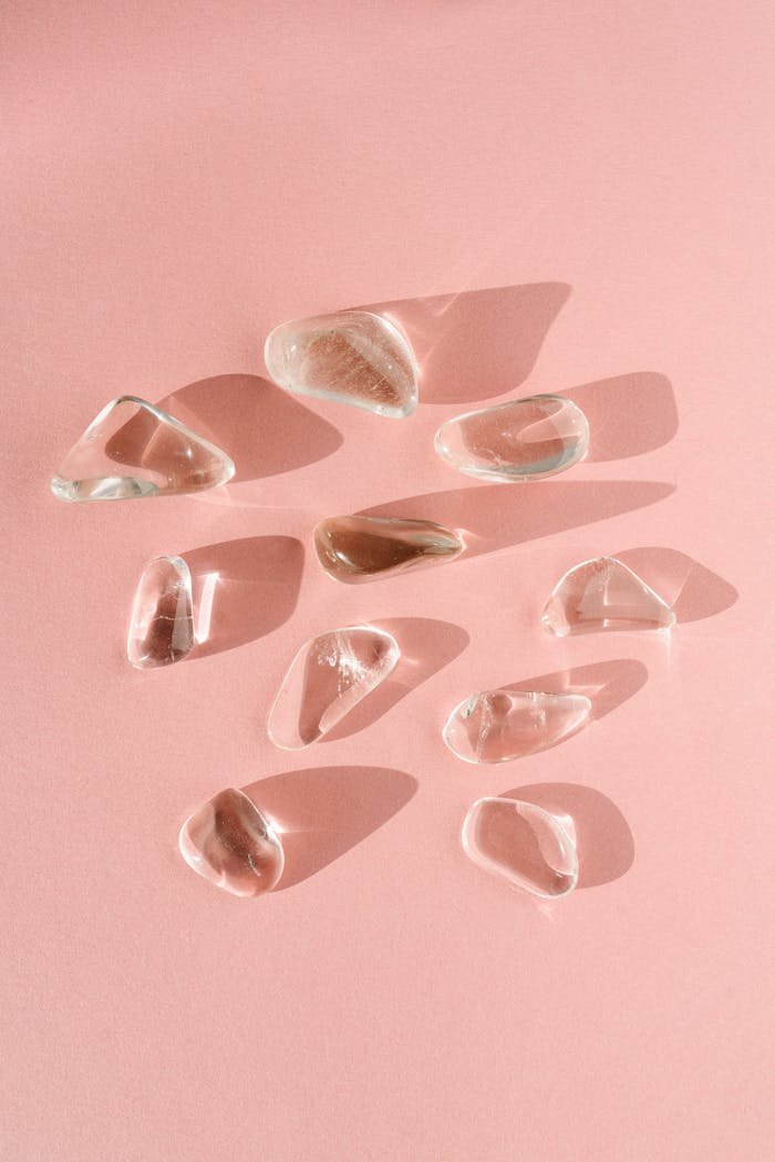 about-01 An artistic arrangement of clear quartz crystals casting shadows on a pink surface.