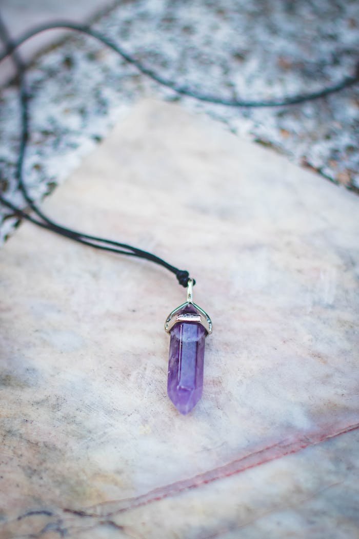 about-02 Close-up of a purple amethyst pendant necklace on marble background.